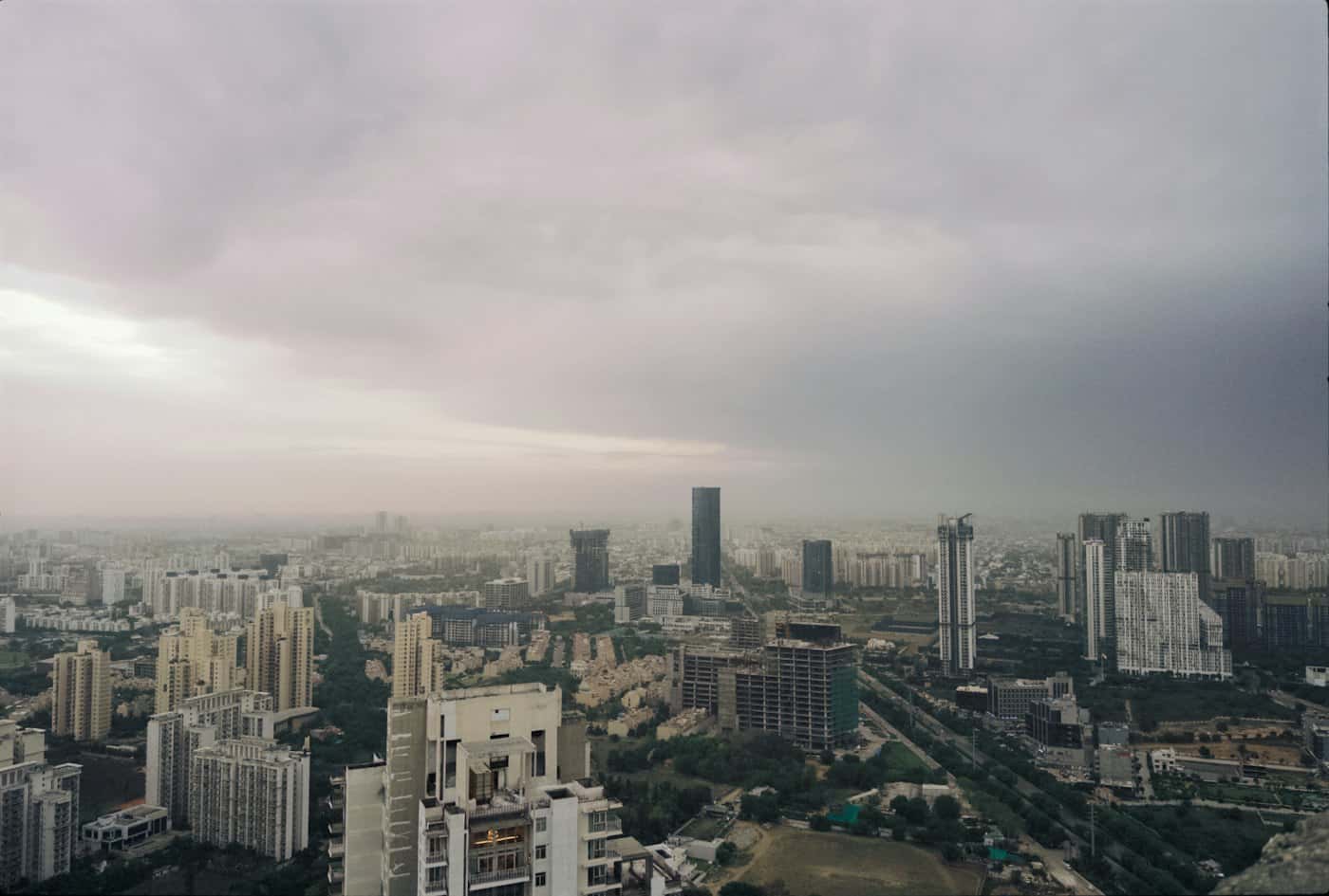 Gurugram skyline from a high-rise: glass office and residential towers under a grey monsoon sky