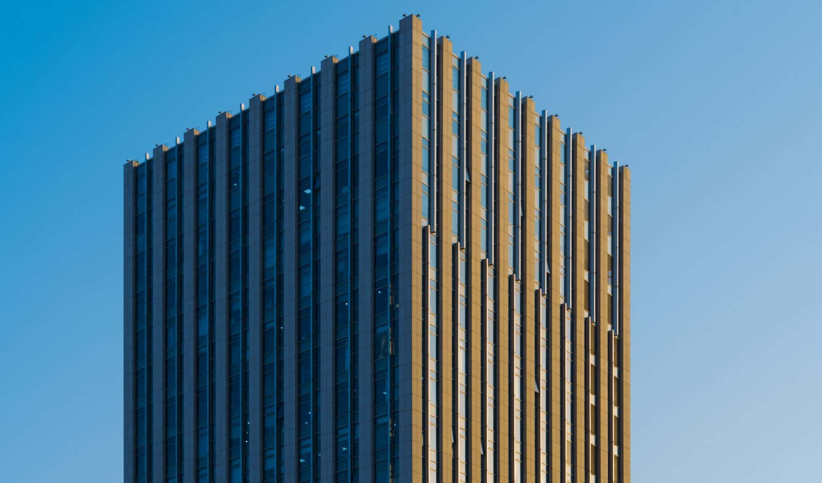 Top of an office tower with bronze and glass vertical fins lit by low sun against a blue sky