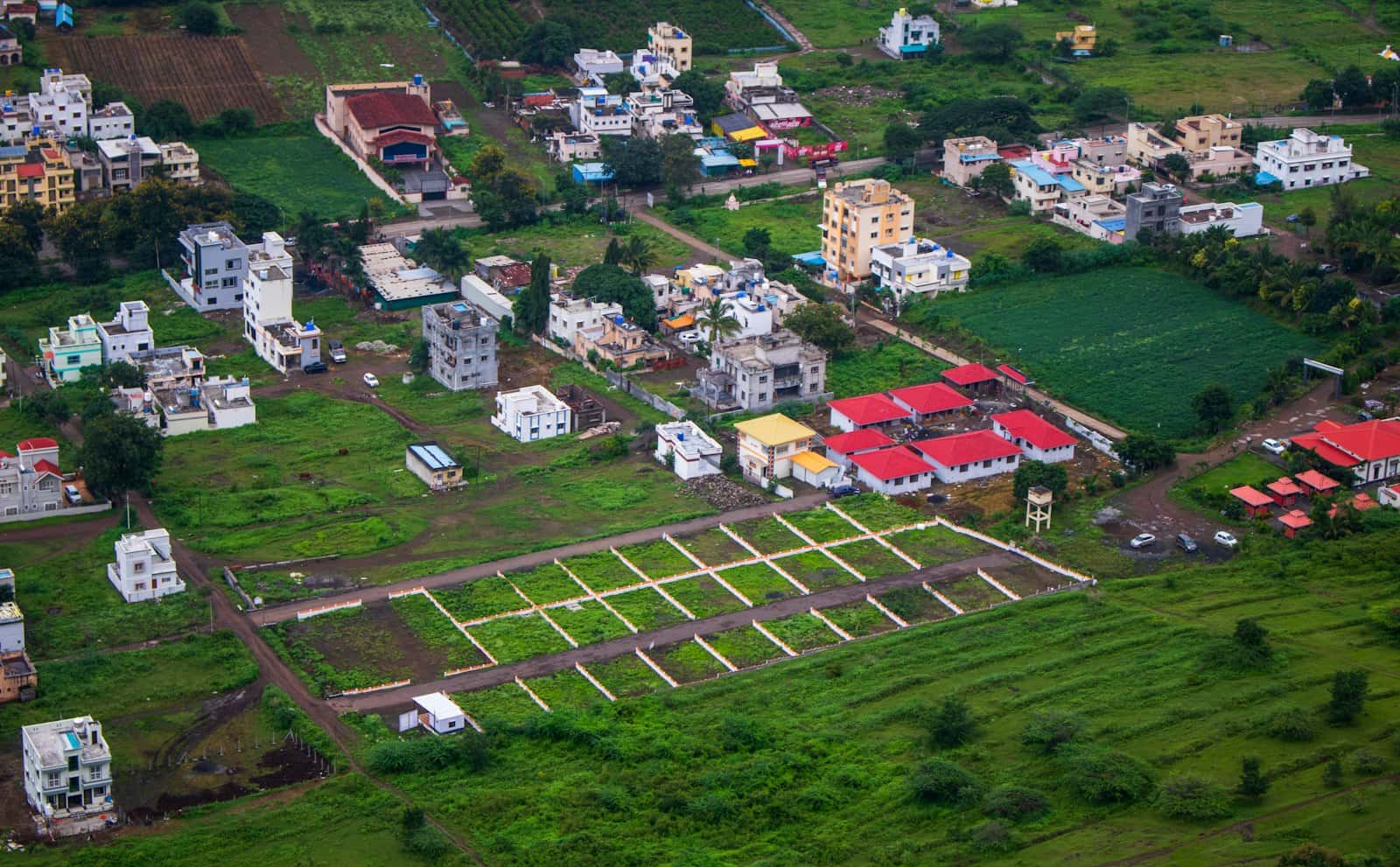 Elevated view of a vacant plot marked out into lots on green open land, beside new houses and low-rise buildings